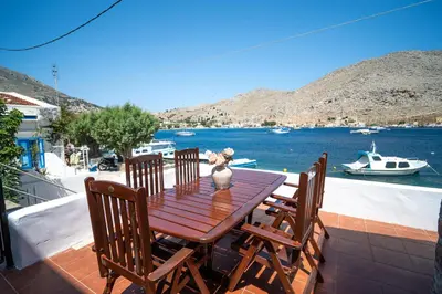 a wooden table and chairs on a deck with a view of the water at Mythos House - Seaside Retreat in Pedi in Symi