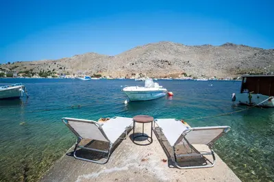 two chairs and a table in the water with a boat at Mythos House - Seaside Retreat in Pedi in Symi
