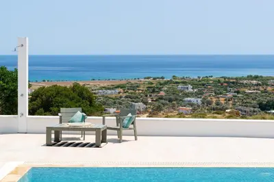 a patio with a table and chairs and the ocean at Hill & Sea View White Pearl Villa in Afantou