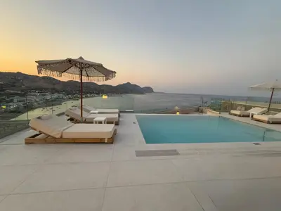 a pool with chairs and an umbrella on a roof at Blue Infinito Boutique Villa, Infinity Pool , Heated Jacuzzi & Panoramic Sea View in Archangelos