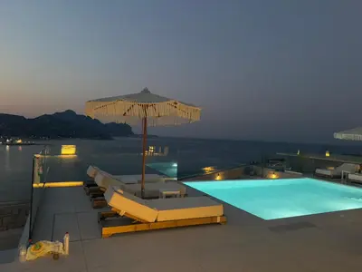 a swimming pool with an umbrella and lounge chairs at Blue Infinito Boutique Villa, Infinity Pool , Heated Jacuzzi & Panoramic Sea View in Archangelos