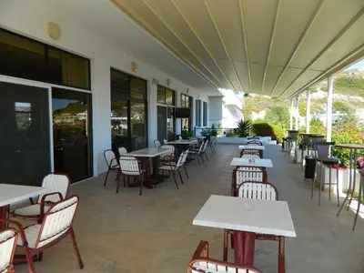 an empty restaurant with tables and chairs and windows at Telhinis Hotel & Apartments in Faliraki
