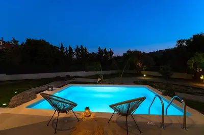 a swimming pool at night with two chairs next to it at SunnyVilla Rhodes in Ialyssos