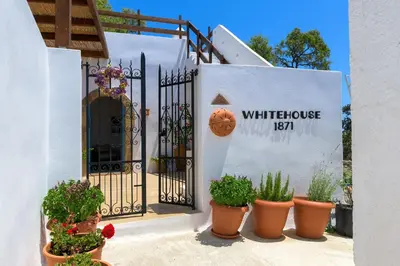 an entrance to a white house with a black gate and potted plants at White House 1871 in Lachania