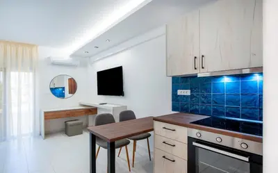 a kitchen with a table and a blue tiled wall at Dorothea Apartments #2 with garden view in Koskinou