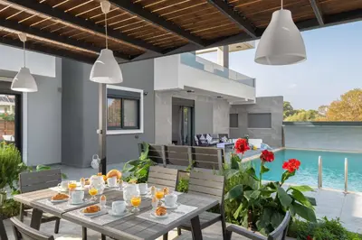 an outdoor dining area with a table and chairs and a pool at Harmony Villas Rhodes in Ialyssos
