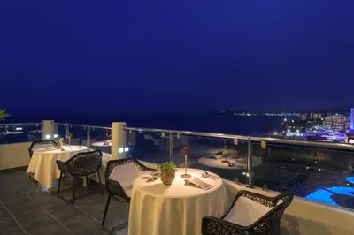 a restaurant with tables and chairs on a balcony at night at Elysium Resort & Spa in Faliraki