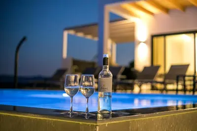 a bottle of wine and two wine glasses next to a swimming pool at Blue Sunrise Villa 2 in Afantou