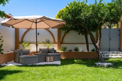 a patio with an umbrella and couches under a tree at Duo Verde Celine Garden Apartment in Kremasti
