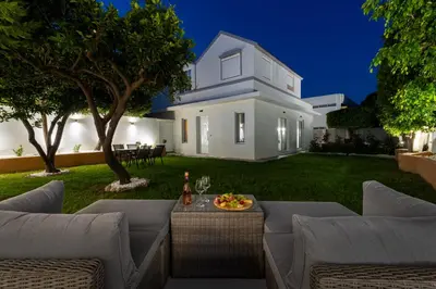 a backyard of a white house with a table and chairs at Duo Verde Celine Garden Apartment in Kremasti