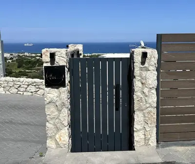 a gate in a stone wall with the ocean behind it at Aelios Petra sea view apartment 4 in Asgourou