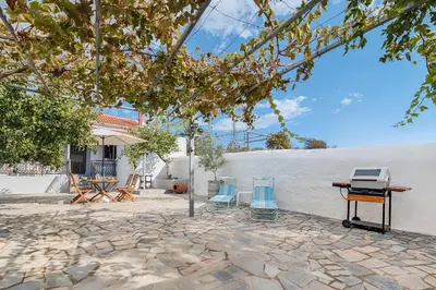 a stone patio with two blue chairs and a white wall at Casa La Perla - Lachania in Lachania
