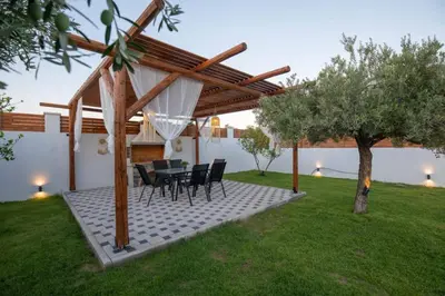 a patio with a table and chairs under a pergola at Garden Olive Luxury Villa in Archangelos