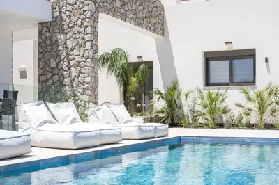 a swimming pool with white furniture next to a house at Nostos Luxury Apartments in Kremasti