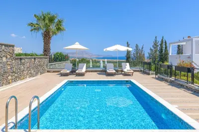 a swimming pool with chairs and umbrellas next to a house at Villa Mariani in Kalathos