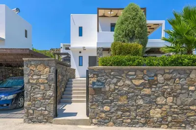 a white house with a stone wall and a car at Villa Mariani in Kalathos
