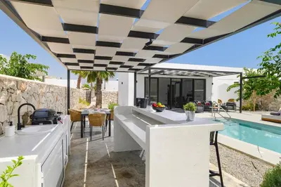an outdoor kitchen and dining area with a pool at Villa Zen Zazan by Villa Plus in Kolimbia