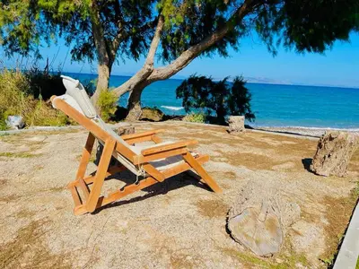 a wooden chair sitting on a beach with the ocean at Villa Ramann, Rhodes in Rhodes Town