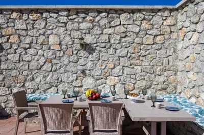 a table with chairs in front of a stone wall at Alki Slow Living Apartments in Rhodes Town