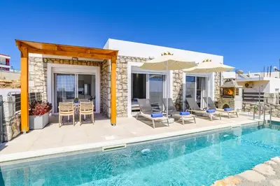 a villa with a swimming pool with chairs and an umbrella at Villa Amethyst Gem by Villa Plus in Gennadi