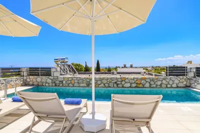 a patio with two chairs and an umbrella next to a pool at Villa Amethyst Gem by Villa Plus in Gennadi