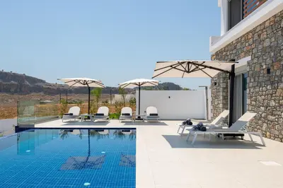 a swimming pool with lounge chairs next to a building at Lindian Poem Villas in Líndos