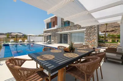 a dining room with a table and chairs and a swimming pool at Lindian Poem Villas in Líndos
