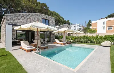a pool with chairs and umbrellas next to a house at Rokas Luxury Villas in Asgourou