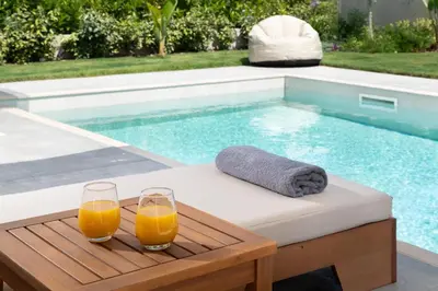 two glasses of orange juice on a table next to a swimming pool at Rokas Luxury Villas in Asgourou