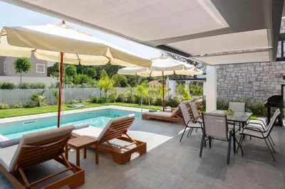 a patio with a table and chairs and a pool at Rokas Luxury Villas in Asgourou