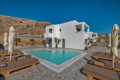 a white villa with a swimming pool and chairs at Amani Villas Lindos in Líndos