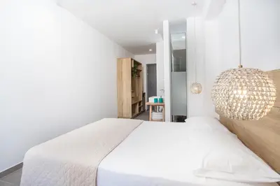 a white bedroom with a large bed and a chandelier at Moscha Hotel in Faliraki