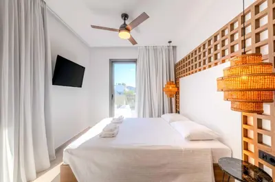 a white bedroom with a bed and a ceiling fan at Alati Suites - Stegna Beach in Vrachonisída touArchangélou