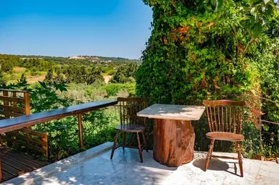 a table and two chairs on a deck with a tree stump at Koskinou Apartments in Koskinou