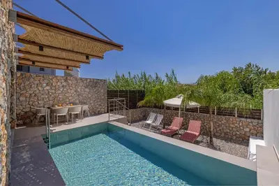 a pool with chairs and a table and a house at Avaton Boutique Suites in Vrachonisída touArchangélou