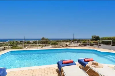 a swimming pool with lounge chairs and the ocean in the background at Villa Phoebe Gennadi in Gennadi