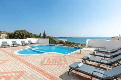 a swimming pool with lounge chairs and the ocean at Pefkos Sea Serenity Villas in Líndos