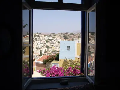 a window with a view of a city with purple flowers at Symi Traditional Appartment in Symi