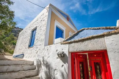 a white building with a red door and stairs at Symi Traditional Appartment in Symi