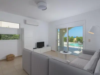 a white living room with a couch and a tv at Holiday Home Liebevoll ausgestattetes Haus in ruhiger Lage mit beheiztem Pool und Meerblick by Interhome in Gennadi