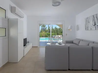 a white living room with a couch and a tv at Holiday Home Liebevoll ausgestattetes Haus in ruhiger Lage mit beheiztem Pool und Meerblick by Interhome in Gennadi