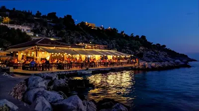 a group of people sitting at a restaurant next to the water at Villa Rafael in Lindos, Rhodos for 8gst in Líndos