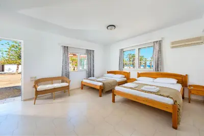 a bedroom with two beds and a chair and windows at Villa Maria Beachfront Residence in Kiotari
