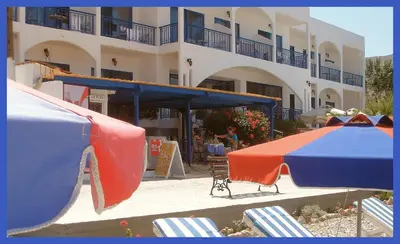 a building with tables and umbrellas in front of it at Hotel Eleni Beach in Livadia