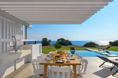 a dining table and chairs on a patio with a pool at Albatross Beach Front Villas in Gennadi