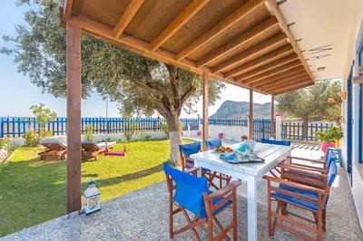 a patio with a white table and blue chairs at Stegna House Sea View in Archangelos