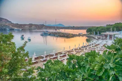 a beach with chairs and boats in the water at Lindos Vigli Private Villa in Líndos