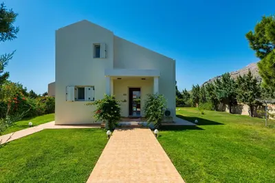 a white house on a green lawn with a pathway at Athena Villa in Kolimbia