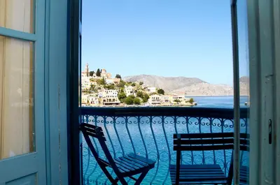 a balcony with a chair and a view of the water at Nireus Hotel in Symi