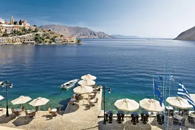 a beach with umbrellas and a boat in the water at Nireus Hotel in Symi